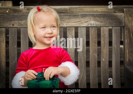 Adorable Little Girl Unwrapping Her Gift on a Bench Outside. Stock Photo