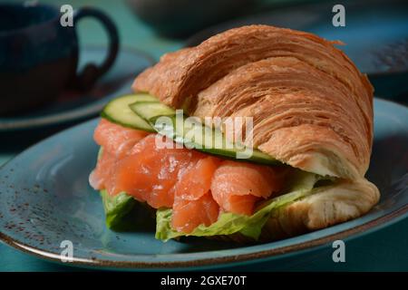 Crispy croissant with salmon and lettuce and cucumbers. Tasty breakfast. Stock Photo