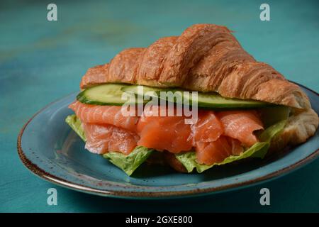 Crispy croissant with salmon and lettuce and cucumbers. Tasty breakfast. Stock Photo