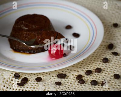 Closeup spoonful of a Coffee Flan on a plate decorated with a cherry and coffee beans Stock Photo