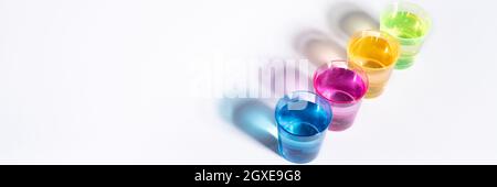 Plastic multi-colored glasses with liquid on a white background with highlights. Layout, mockup. Stock Photo