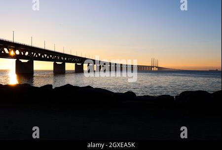 Sun seen through the Oresund bridge at the viewpoint near Limhamn, Sweden, in February 2021. Wide angle, clear sky, bridge stretching from the left to Stock Photo