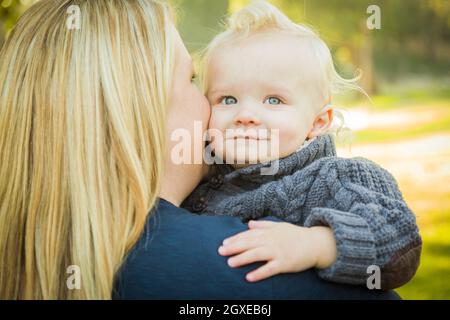 Mother Embracing Her Adorable Blonde Haired Blue Eyed Baby Boy Outdoors. Stock Photo