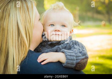 Mother Embracing Her Adorable Blonde Haired Blue Eyed Baby Boy Outdoors. Stock Photo