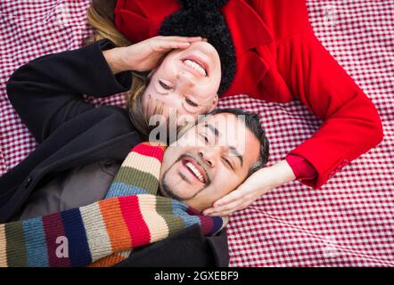 Young Mixed Race Couple Wearing Winter Clothing on Blanket in Park. Stock Photo