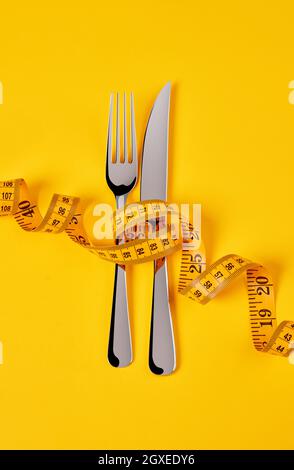 Knife and fork with measuring tape on yellow background Stock Photo