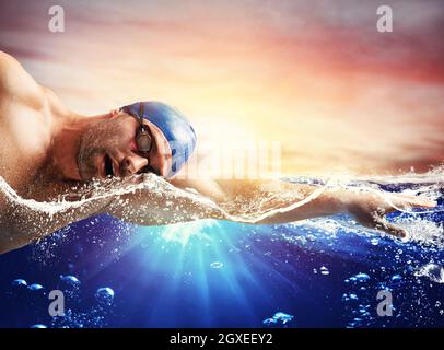 Boy swims in a blue deep water during sunrise Stock Photo