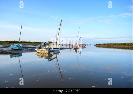Sailboats and small leisure boats moored on Morston Creek near Blakeney Point while tide is coming in on a bright late afternoon. Norfolk, England. Stock Photo