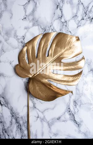 Golden monstera leaf on luxury marble background. Clean minimal flat lay design. Tropical gold foliage for trendy layout. Luxury fashion lifestyle con Stock Photo