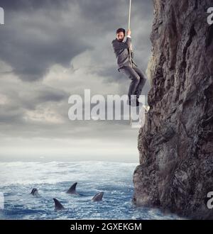 Businessman is likely to fall into the deep sea with sharks. concept of problems and difficulty in business Stock Photo