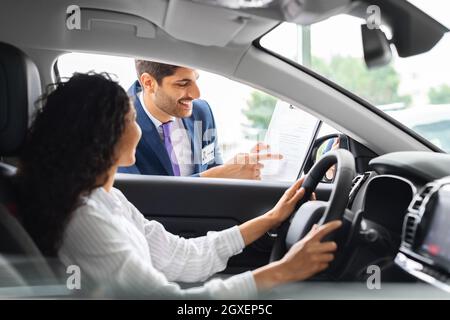Young woman sitting inside car, having conversation with sales manager Stock Photo