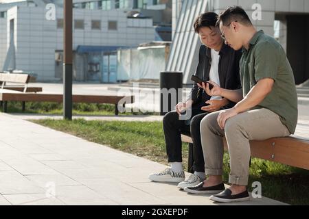 Two young Chinese businessmen looking through data on smartphone screen Stock Photo