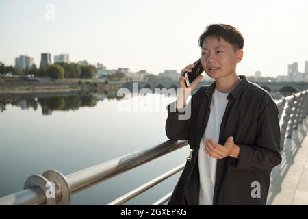 Young Asian businesswoman in smart casualwear talking on mobile phone in urban environment Stock Photo