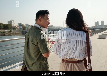 Rear view of two young Chinese colleagues taking walk along riverside and interacting Stock Photo