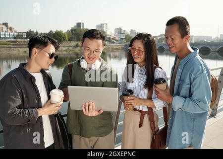 Four young Chinese colleagues with laptop working in the net outdoors Stock Photo