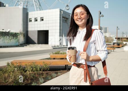 Young successful businesswoman with drink looking at you during walk on sunny day Stock Photo