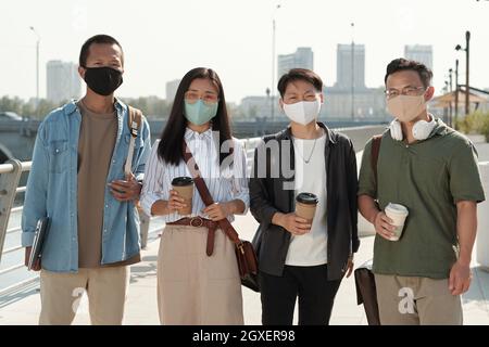 Group of young Chinese businesspeople in protective masks holding drinks Stock Photo