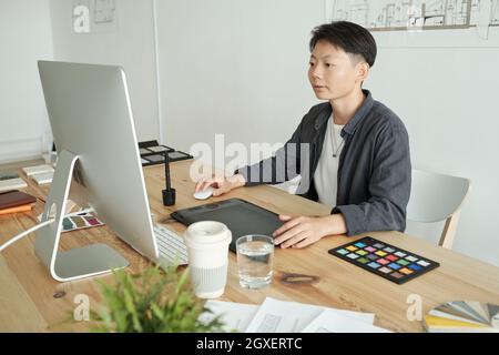 Young Chinese female designer sitting in front of computer monitor by desk in office Stock Photo