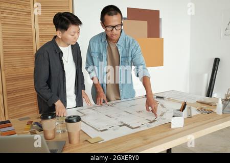 Two young Chinese engineers in casualwear discussing sketch on blueprint Stock Photo