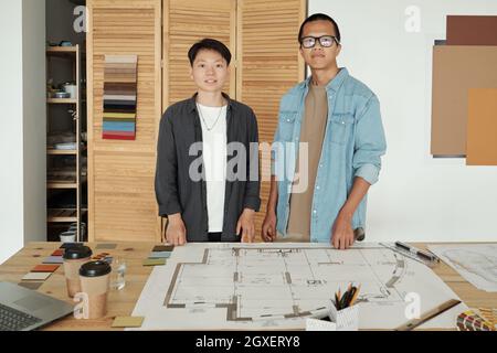 Two young successful engineers in casualwear standing by workplace in office Stock Photo