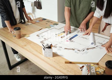 Team of contemporary engineers discussing color palette over blueprint with sketch Stock Photo