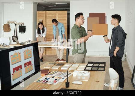 Two office workers with drinks discussing working points by workplace at coffee break Stock Photo