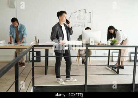 Young businesswoman with blueprint calling in working environment in office Stock Photo