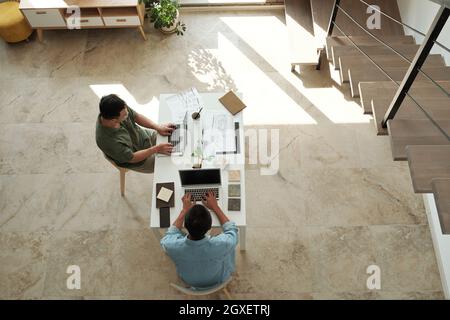 Two young designers or architects typing on laptops while sitting by table in office Stock Photo