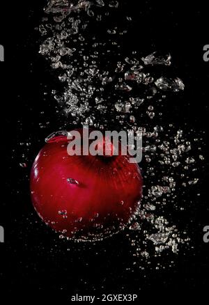 Red onion splashing in water on a black background Stock Photo