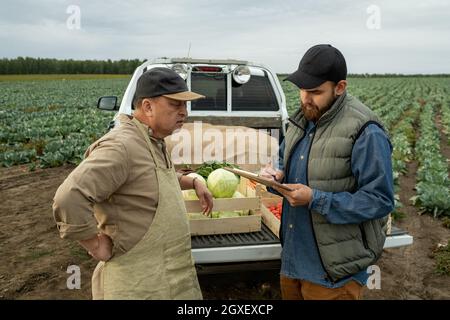 Mature farmer talking to young bearded man making notes in document Stock Photo