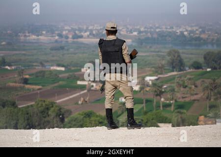 The rear view of an Egyptian security soldier, holding a rifle, looking out over the Nile Valley, from the rock cut tombs at Beni Hassan. Stock Photo