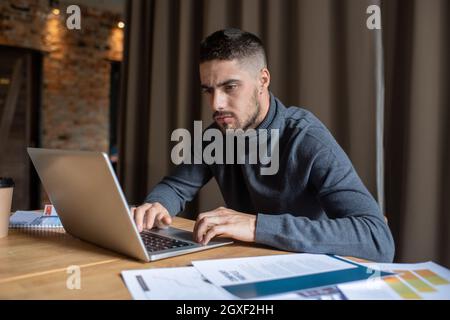 Serious male freelancer concentrating on remote work while sitting in front of laptop Stock Photo