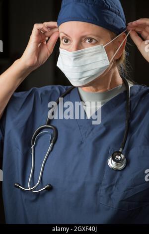 Attractive Female Doctor or Nurse Putting on Protective Face Mask. Stock Photo