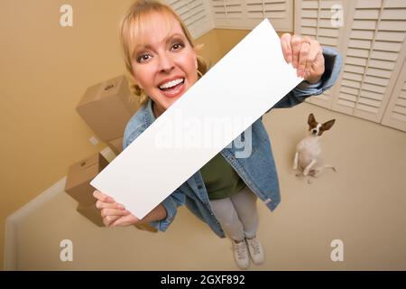 Excited Woman and Doggy with Blank Sign Near Moving Boxes in Empty Room Taken with Extreme Wide Angle Lens. Stock Photo
