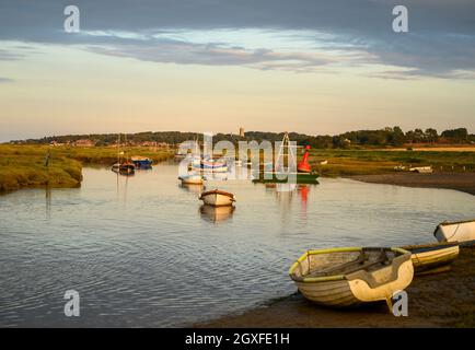 View from Morston Quay towards Blakeney village and church with small boats moored on Morston Creek in warm evening sunshine, Norfolk, England. Stock Photo