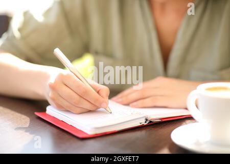 Front view close up of a woman hand writing on paper agenda in a coffee shop Stock Photo