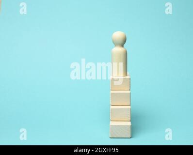 a wooden figurine of a man stands on a ladder of blocks at the very top. The concept of achieving the set goals in business, career growth. Blue backg Stock Photo
