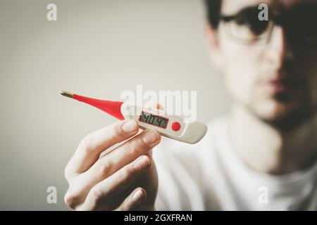 Man holds a red fever thermometer with high temperature in his hand, blurry face Stock Photo