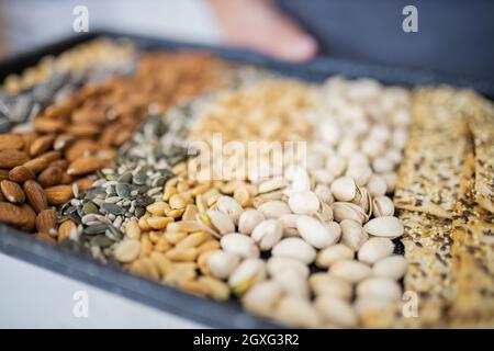 Male hands holding black tray of chickpeas, almonds, peanuts, pistachios, and multi-seed crispbread. Fresh crispy bread, seeds, and nuts. Healthy snac Stock Photo