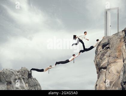 Businessmen working together to form a bridge between two mountains to reach a door. concept of ambition in business Stock Photo
