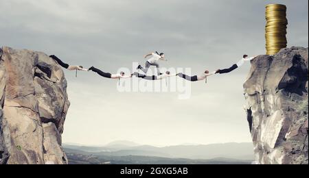 Businessmen working together to form a bridge between two mountains to get the money Stock Photo