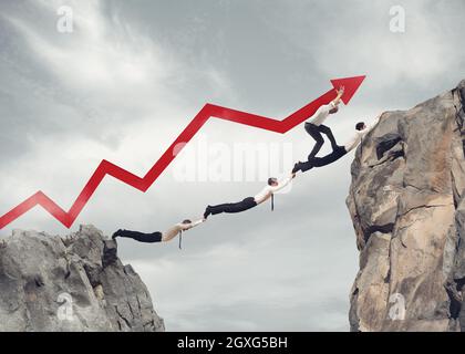 Businessmen working together to form a bridge between two mountains and raising an arrow Stock Photo