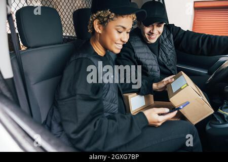 Two couriers sitting in car checking information on box using mobile phone Stock Photo