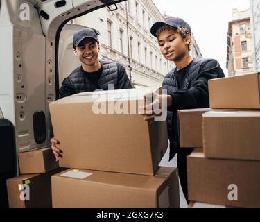 Two workers of delivery company loads cardboard boxes into a van Stock Photo