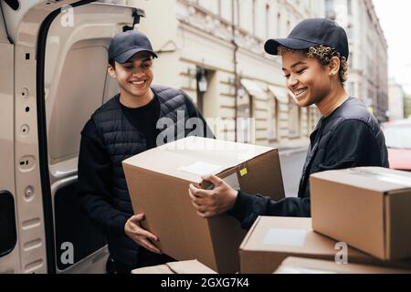 Two smiling couriers unloading cardboard boxes from van in the city Stock Photo