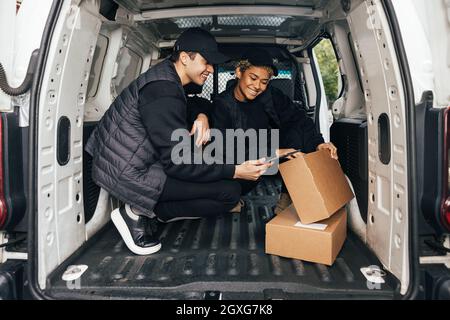 Two smiling couriers sitting in delivery van checking information on a box using digital tablet Stock Photo