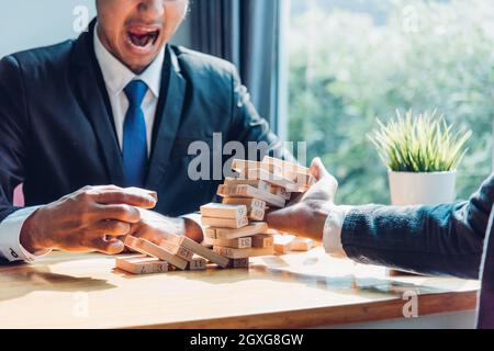 Business man strategy risk pulling block wood tower and have one businessman help to support Stock Photo