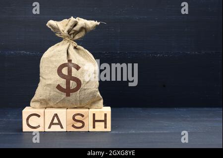 brown full canvas bag with dollar symbol and wooden cubes with the inscription cash. The concept of tax evasion, accumulation and saving. Blue backgro Stock Photo