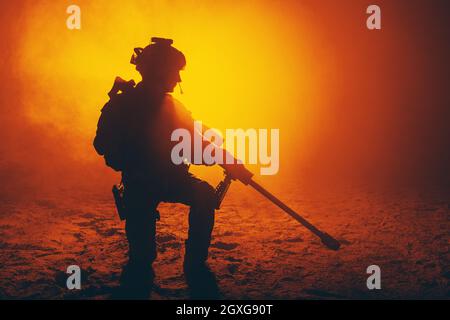 Army sniper with large caliber rifle sitting in the fire and smoke. Backlit silhouette, toned image Stock Photo