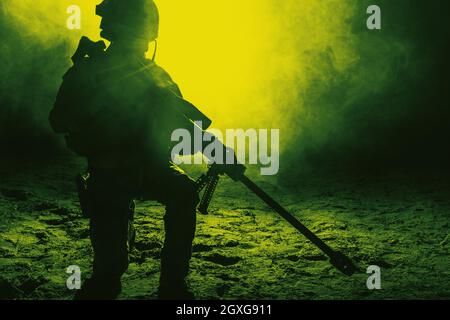 Army sniper with large caliber rifle sitting in the fire and smoke. Backlit silhouette, toned image Stock Photo